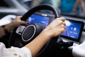 Female hands holding the steering wheel of a modern electric car With digital screen to help the driver