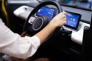 Female hands holding the steering wheel of a modern electric car With digital screen to help the...