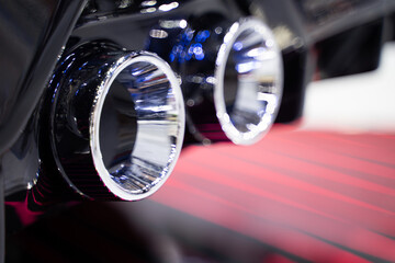 Dual chrome exhaust pipes of a powerful black sports car bumper, bokeh light background