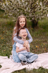 Portrait of a boy and a girl in the park. Brother hugging sister in the park against the background of green trees and apple flowers, friendship concept.