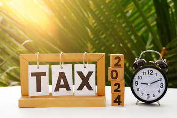 2024 number on a wooden block cube and tax text on paper stand frame with vintage  alarm clock on...