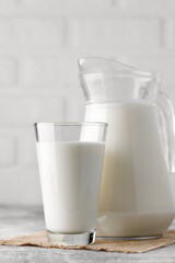 jug and glass of milk on table with white brick wall as background