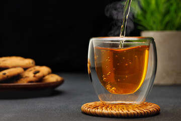 hot tea pouring from teapot into glass cup on table