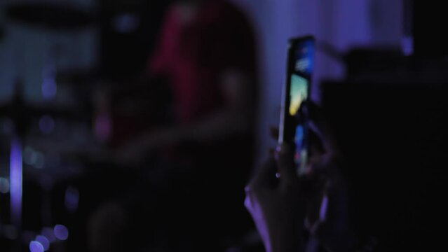 Close-up of a smartphone screen in the hands of a female fan at a rock concert. The girl shoots the performance of the band. On the stage bright flashes of light show