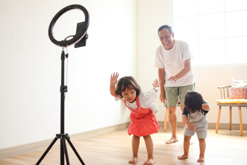 Asian children with grandpa dancing at camera filming video using phone on tripod at home, creating trendy content for social media