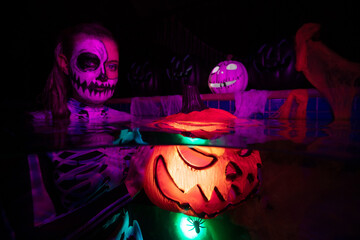 Halloween women holding a colourful pumpkin underwater in a pool with candys, skulls and spiders 