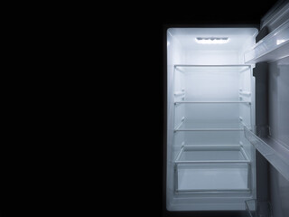 interior of refrigerator with the door open on black background with light in the upper area inside the refrigerator