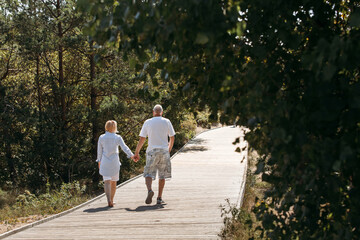 Fototapeta premium Happy elderly couple walking on a wooden deck on a forest path in the sand dunes