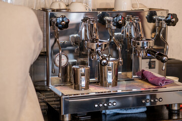 The barista prepares fresh coffee in the coffee machine in the morning in the cafe. There are coffee cups on the table for customers. Coffee machine close-up