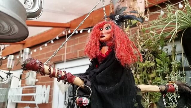 Hand crafted red haired witch hanging from broomstick in home garden outdoor shelter