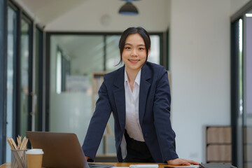 An Asian businesswoman standing and using a laptop computer at an office.