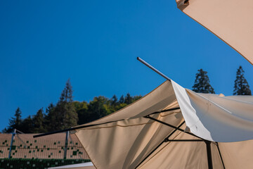 Broken sun umbrella or sunshade at a resort. Beautiful white umbrella for protecting from harsh sun is broken. Blue sky in the background.