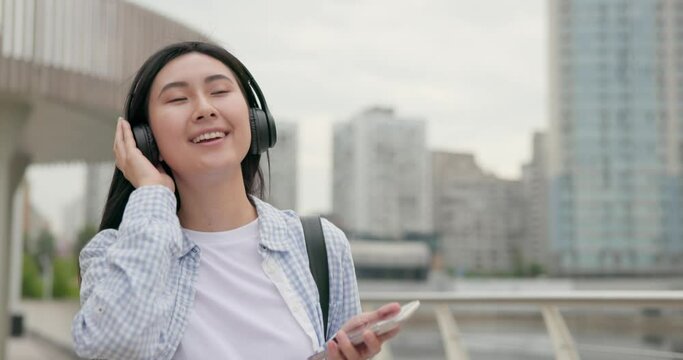 Attractive young asian woman with headphones walking at the city