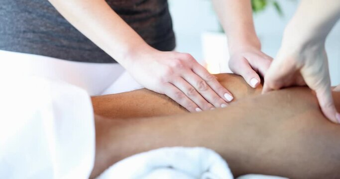 Masseuses doing foot massage to client in beauty salon closeup. Pain in calf area causes in men