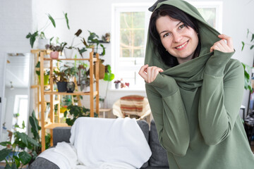 Large portrait Joyful emotions of a woman in the hood in her home in a bright modern interior with home plants. Eco-friendly portrait with real joy