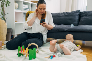 Mother is using mobile phone while her baby plays on the floor.