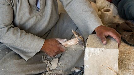 A man traditionally creating Egyptian sculptures by hand with stone chips flying off