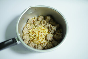 Yellow istan noodles and meatballs are ready to be cooked in a pot on a plain background