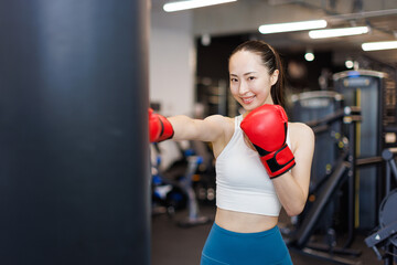 ボクシンググローブとパンチングバッグでトレーニングする若いアジアの女性 - obrazy, fototapety, plakaty