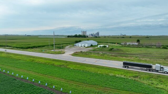 Semi truck with trailer full of corn, grains, and animal feed driving on country roads in midwest USA in summer. Aerial tracking shot of transportation of crops from breadbasket of America.