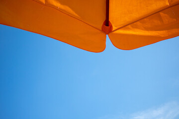 Vivid orange umbrella beach with bright blue sky.