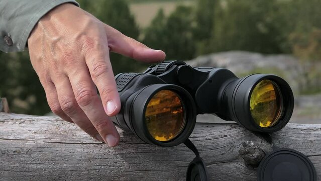 Man picking up binoculars on fallen tree with nature hill forest wilderness view