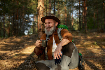 Happy smiling relaxed mature hiker drinking hot tea during hiking outside