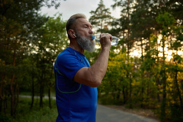 Mature retired man runner taking break drinking water during training