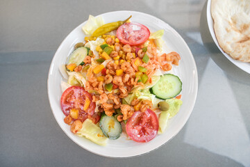 salad of shrimps, tomatoes, cucumbers and lettuce with a yogurt sauce on a white plate and a gray table, high angle view from above