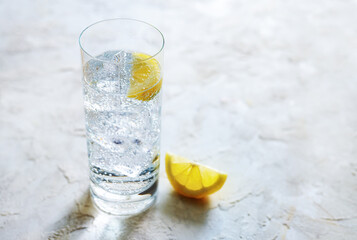 Fresh carbonated mineral water with ice cubes and lemon slices in a drinking glass, refreshing...
