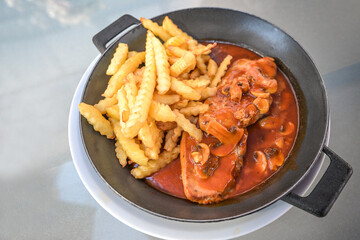 Steak from pork with mushroom, tomato sauce and French fries in an iron pan, meat dish for lunch or dinner, selected focus,