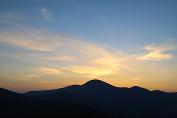 dark silhouette of a mountain against a background of clouds shining gold in the first rays of the sun at dawn