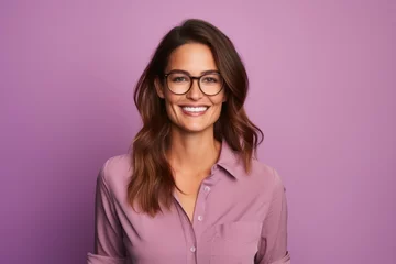 Fotobehang Portrait of beautiful young woman in eyeglasses looking at camera and smiling while standing against purple background © igolaizola