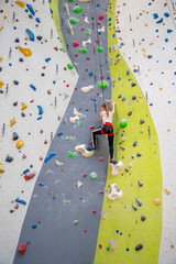 Rock climber young woman hanging on colored hooks on climbing artificial wall indoors of sport centre of Prague. Extreme sports and bouldering concept