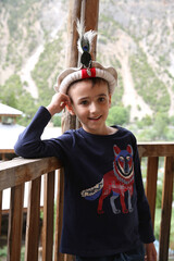 Tourist child, portrait of cute boy, fun kid, toddler in beautiful mountains in Chitral, Pakistan. Tourist child in traditional national folk hat, costume. Fashion boy in mountains. Nature of Pakistan