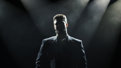Silhouette of a handsome, stylish man posing on a dark background in a business suit