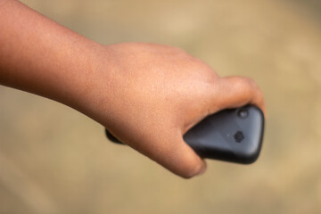 A human hand holds a small mobile phone and the background blur