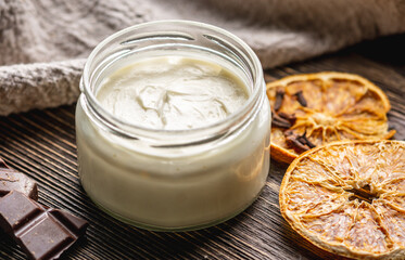 Natural fragrant cream or butter for body in a clear glass jar on a wooden background. Concept of organic cosmetics and skin care