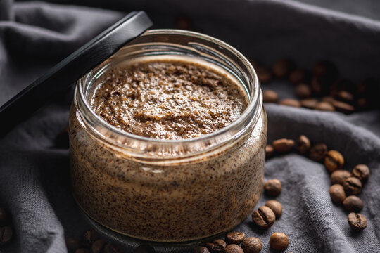 Organic oil scrub with sugar and coffee on the background of coffee beans on black cloth. Concept of natural cosmetics and skin care