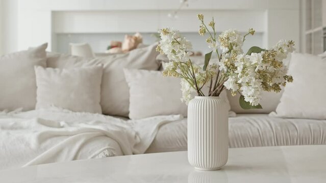 Medium shot of trendy minimalist vase with flowers on coffee table beside sofa in white living room with no people there