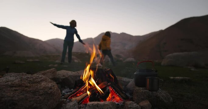 Mom with child campfire flame twilight. Mom and son playing and having fun in background. Happy family. They play airplanes, run after each other in circle, arms outstretched to the sides. Mountains