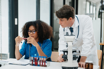 Focused mature male doctor and African female nurse look at tablet and laptop screen discuss anamnesis together. Concentrated diverse medical professionals