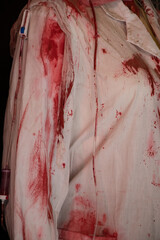 A bloody white medical gown of a nurse, covered in blood and a drip, hangs on the gown, a doctor's...