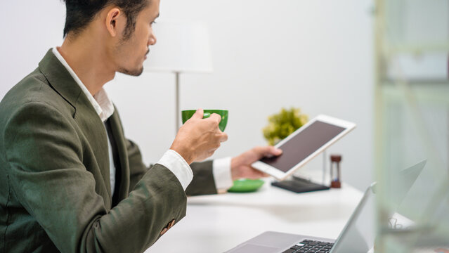 The manager of an Asian man sipping coffee on his desk in a radiant manner.
