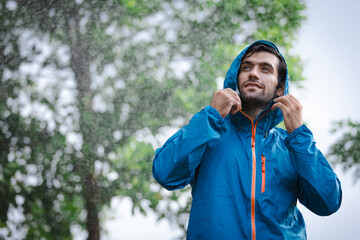 man in a raincoat in the rain in a rainy day in the park, the concept of the rainy season