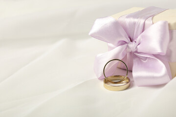 Gift box and wedding rings on light background, space for textGift box and wedding rings on light background, space for text