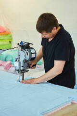 A man works on a machine for cutting fabrics in textile production. Tailoring.
