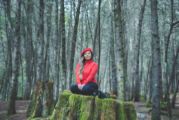 Naklejka na ściany i meble Woman in a calm and thoughtful attitude on a mossy stump in the middle of the forest.
