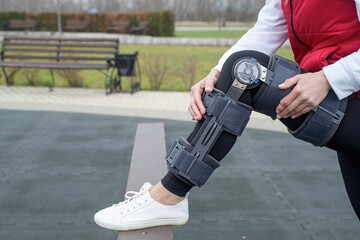 Woman wearing knee brace or orthosis after leg surgery, walking in the park