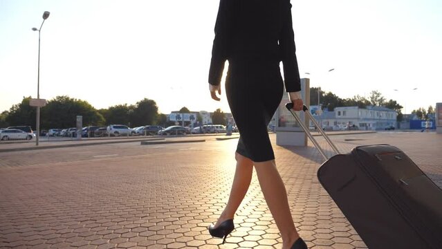 Business woman walking with her suitcase from airport hall or waiting room. Young girl in heels going from terminal and rolling luggage on wheels. Business lady stepping at city street. Slow motion